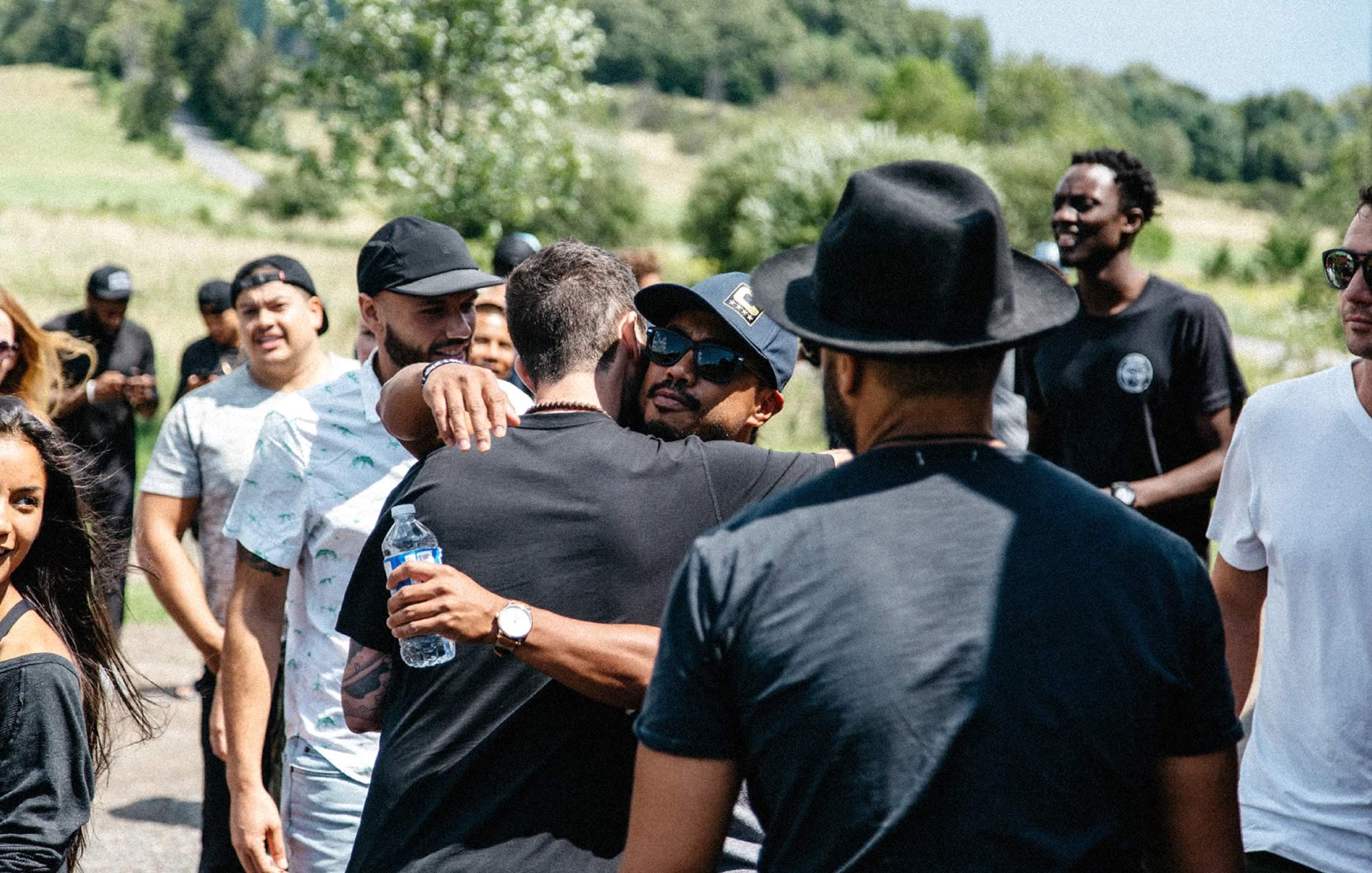 Image of two men hugging amongst a larger crowd of young adults (upon completion of an outdoor trek)